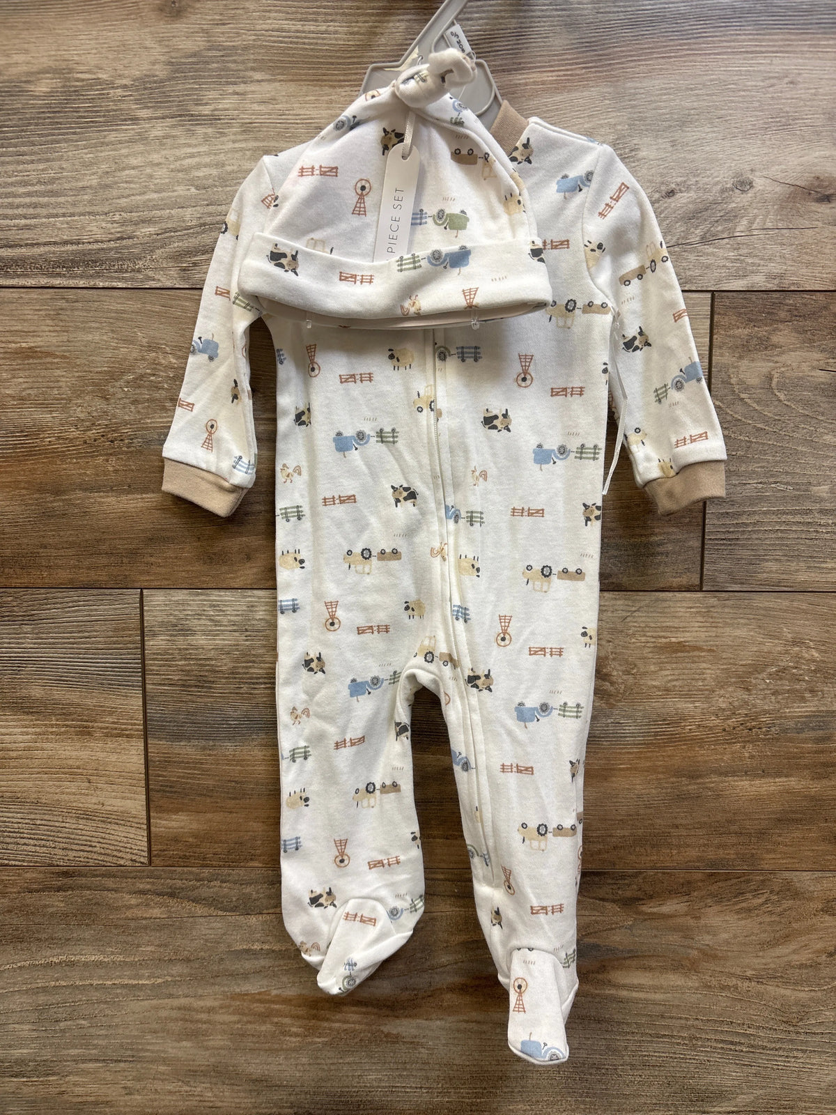 Flat lay of Kyle and Deena 2pc white sleeper and hat set showcasing farm animal print, full zipper, and footed design