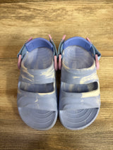 Overhead view of light blue Rugged Shark toddler sandals with marbled pattern, two straps and textured footbeds on wood