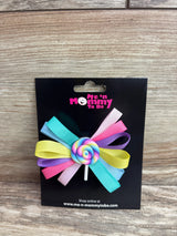 Front view of lollipop applique hair bow showcasing multicolor ribbon loops and rainbow lollipop center on a black display card with Me 'n Mommy To Be logo