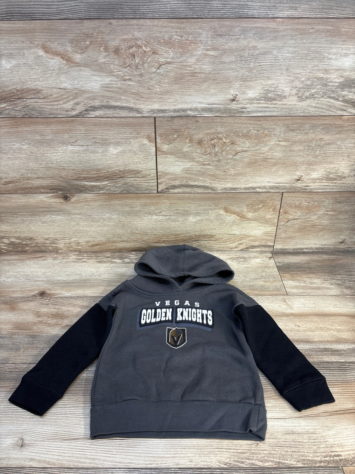 Kids Vegas Golden Knights hoodie, gray with black sleeves, laid on wood floor