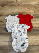 Top-down view of Nautica 3-pack bodysuits showing sailboat-print, white with tiny navy motifs, and solid red on wood floor