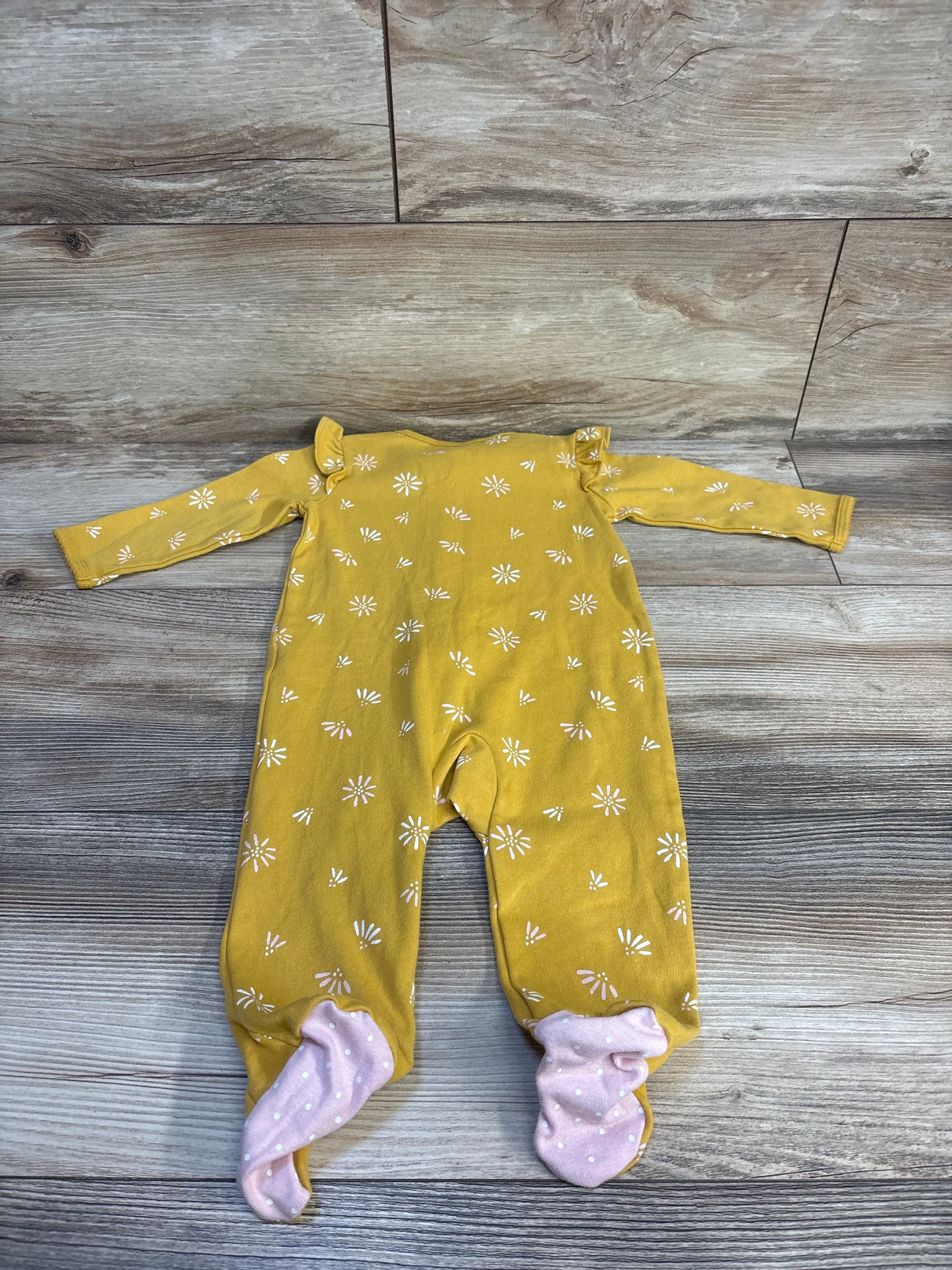 Mustard yellow baby onesie with white daisy print and pink polka dot footies, laid on wood floor