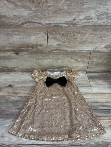 Front view of a gold Zunie sequin embellished A-line dress with a black bow and short sleeves on a wood plank background