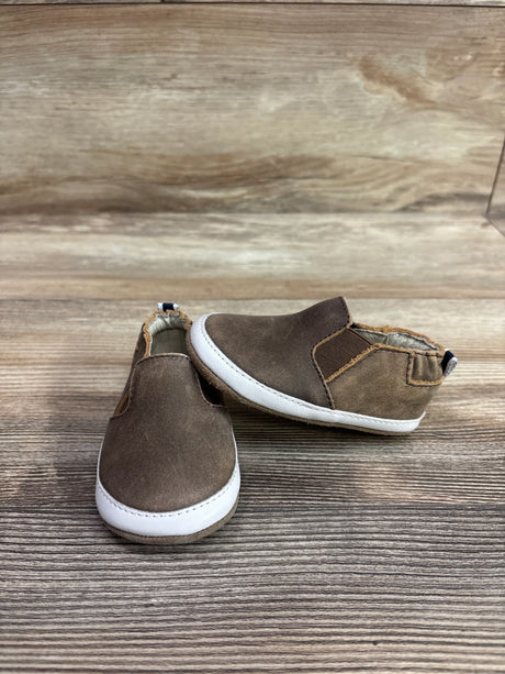 Pair of brown Robeez Lenny Loafer crib shoes with white soles on a wooden surface.