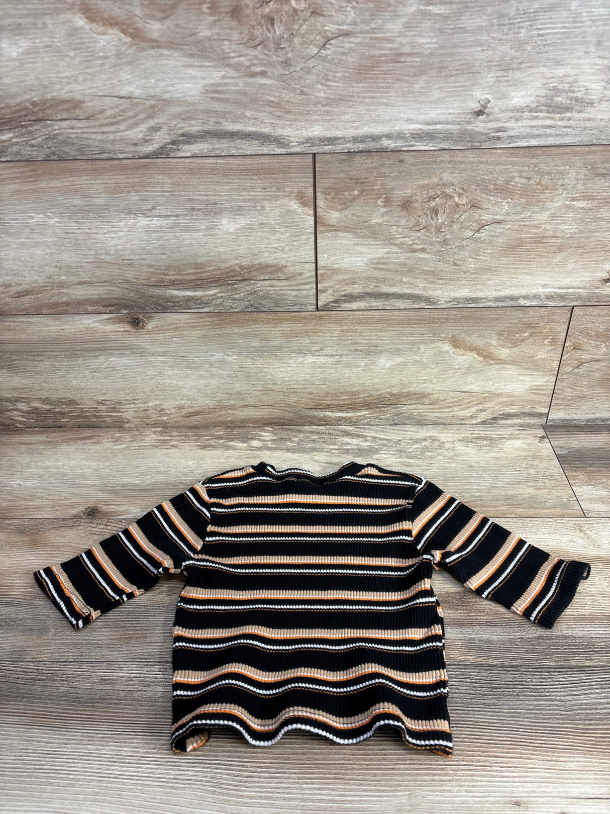 Children's long sleeve ribbed shirt with black, brown, and white stripes on wood background