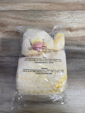 Yellow and white plush stuffed animal in clear plastic packaging on wooden surface, children's toy