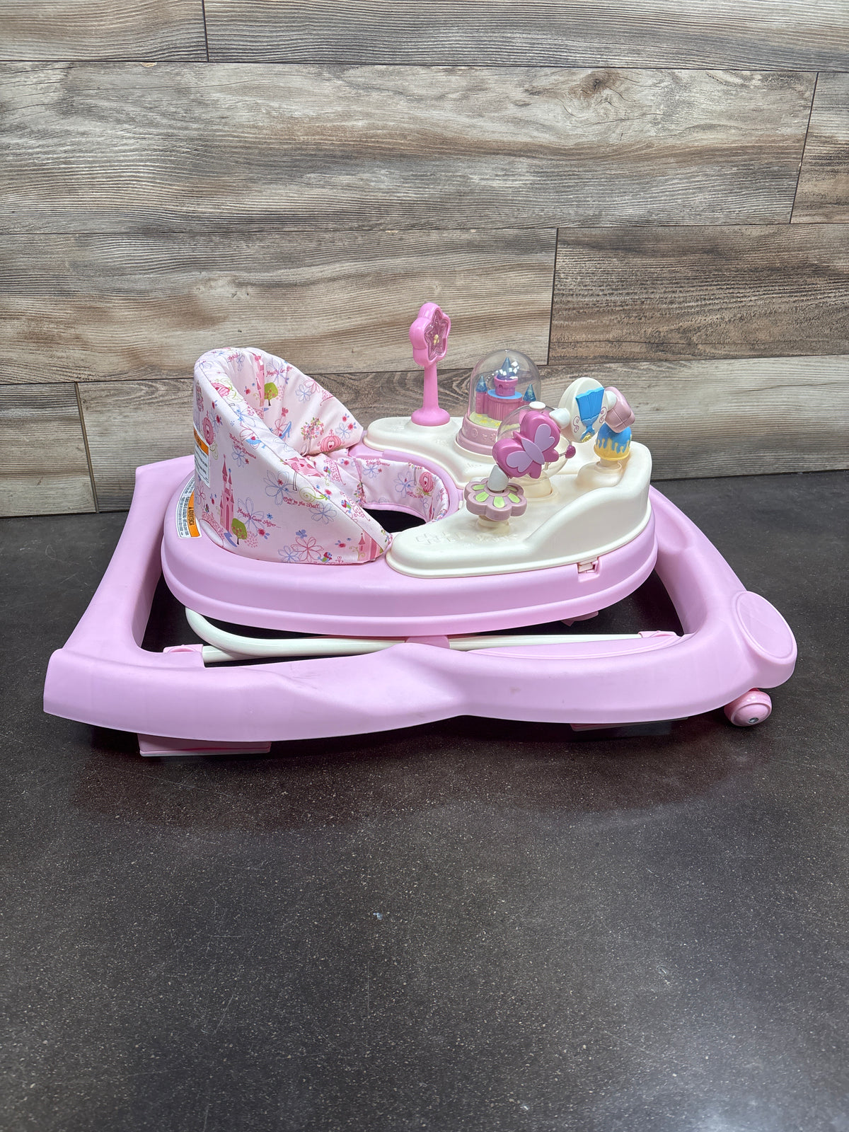 Front view of Disney Music and Lights Baby Walker showcasing pink floral seat and activity toys on wood backdrop