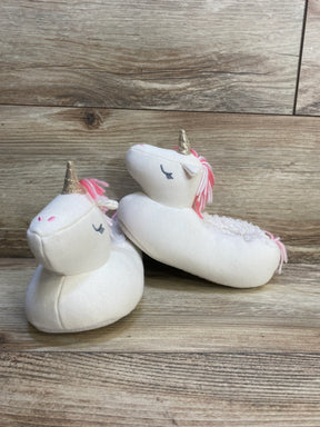 Plush unicorn baby slippers with gold horns and pink manes on wood background