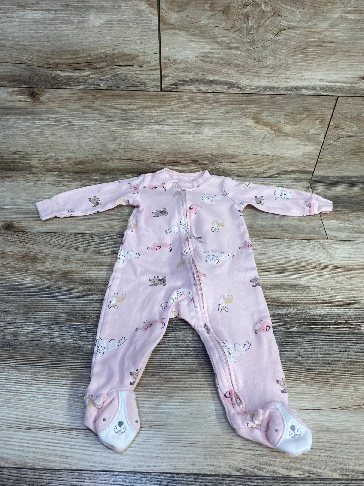 Top-down view of pink Carter's footed baby sleeper size 9M showcasing dog-face feet and all-over animal print on wood floor