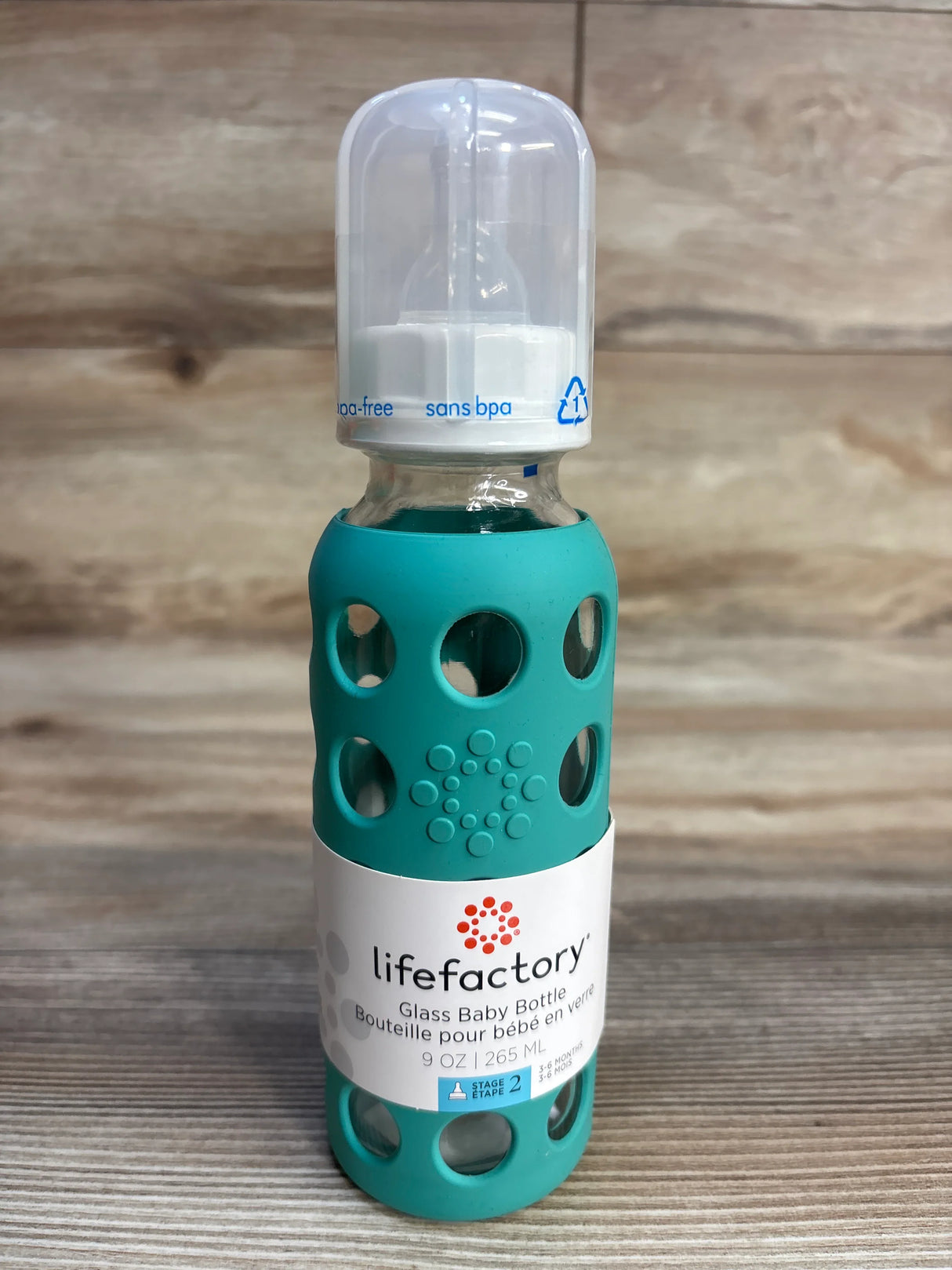 Lifefactory glass baby bottle with teal silicone sleeve and BPA-free cap on wood surface