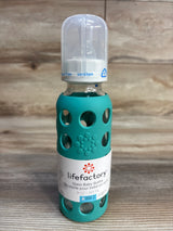 Lifefactory glass baby bottle with teal silicone sleeve and BPA-free cap on wood surface
