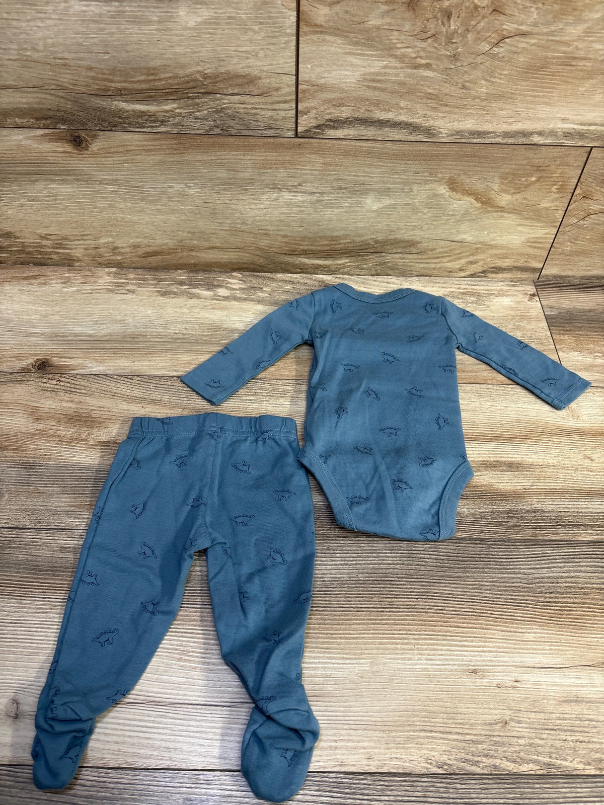 Top-down view of blue dinosaur-print kimono bodysuit and footed pants showcasing long sleeves and footed feet on a wood floor