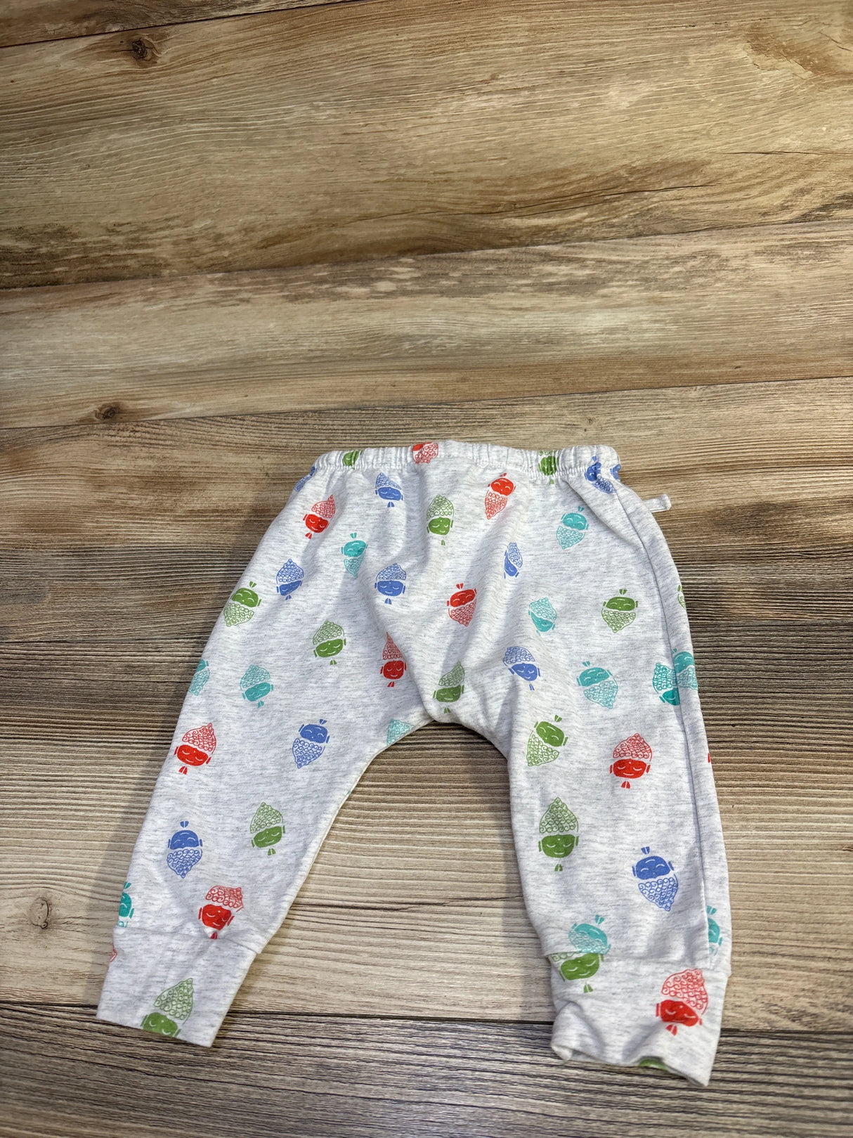 Flat lay of grey baby harem pants showing multicolored acorn print, elastic waistband and cuffed ankles on wood background