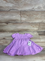 Flat lay of purple Okie Dokie tiered baby dress and matching bloomers showing short puff sleeves and ruffled tiers on a light wood floor