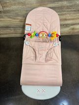 Overhead view of Baby Bjorn bouncer in dusty pink quilted petal fabric with colorful toy bar and front harness on wood floor