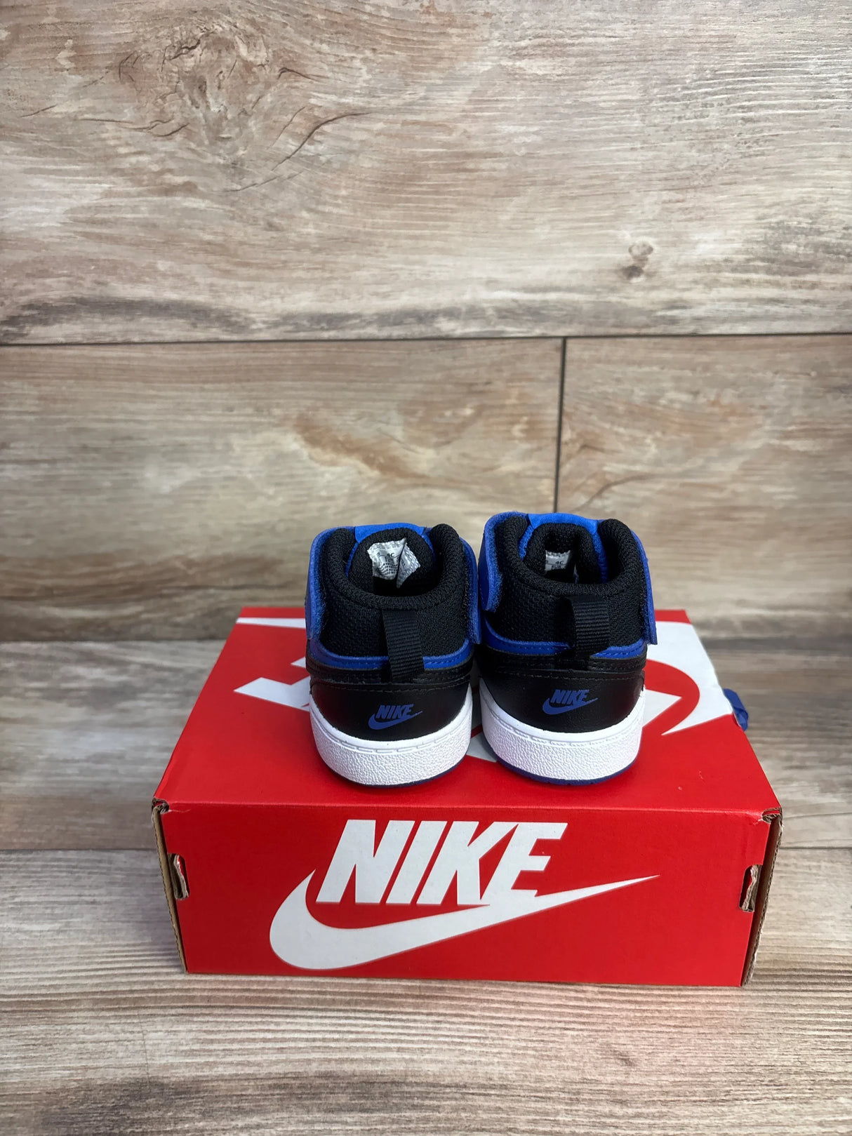 Rear view of toddler Nike Court Borough sneakers in black and game royal with Velcro on red Nike box