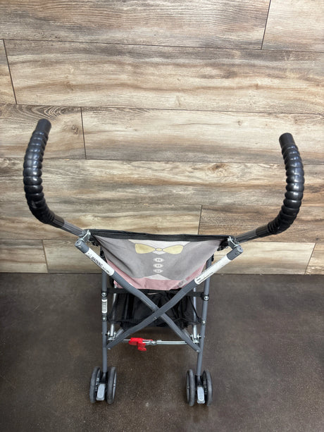 Rear view of Cosco umbrella stroller showing black curved handles, metal frame, pink-and-gray seat with yellow bow, underseat basket