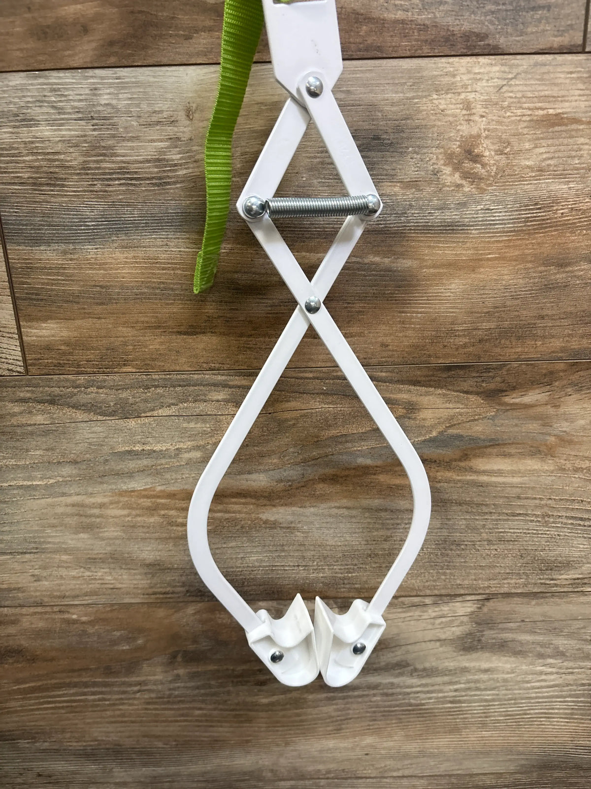 Top down view of Evenflo Exersaucer Door Jumper showing white frame, spring mechanism, and green strap on wood flooring