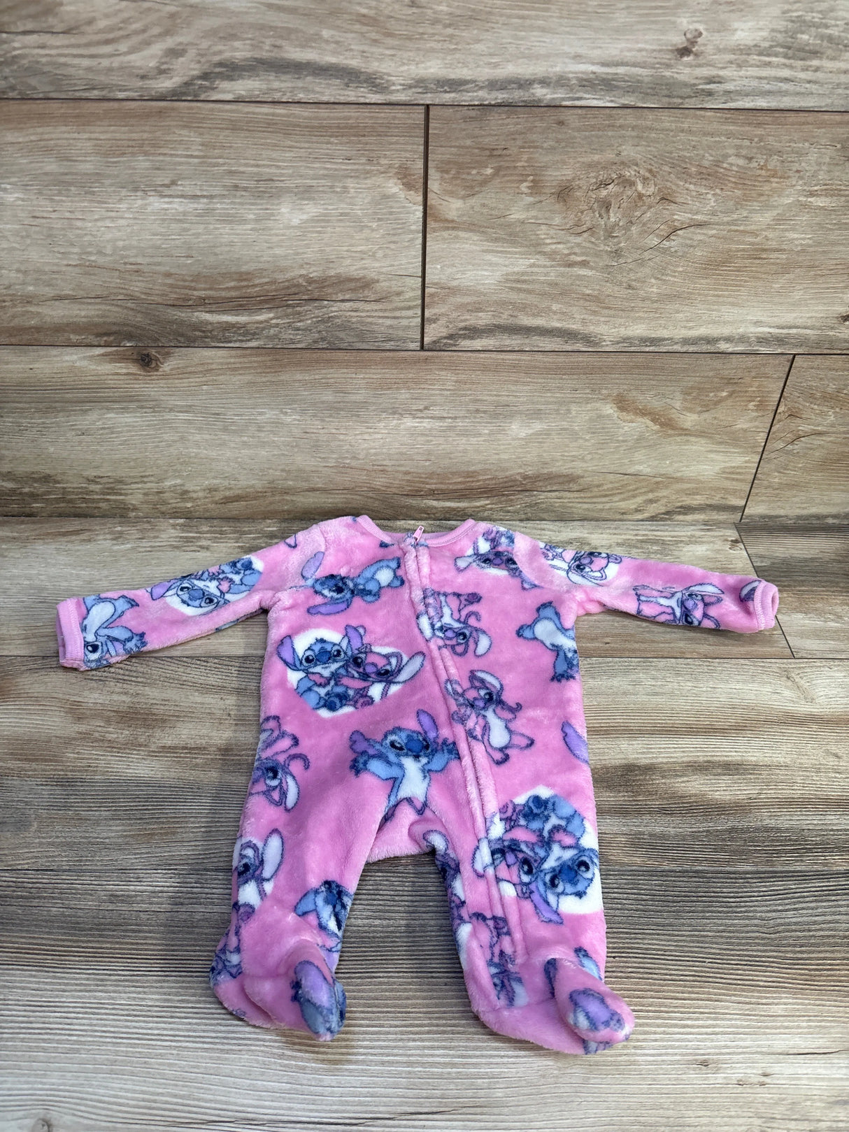 Front flat-lay of pink Disney Lilo & Stitch footed sleeper size 0-3 months showing plush fleece fabric on wood background