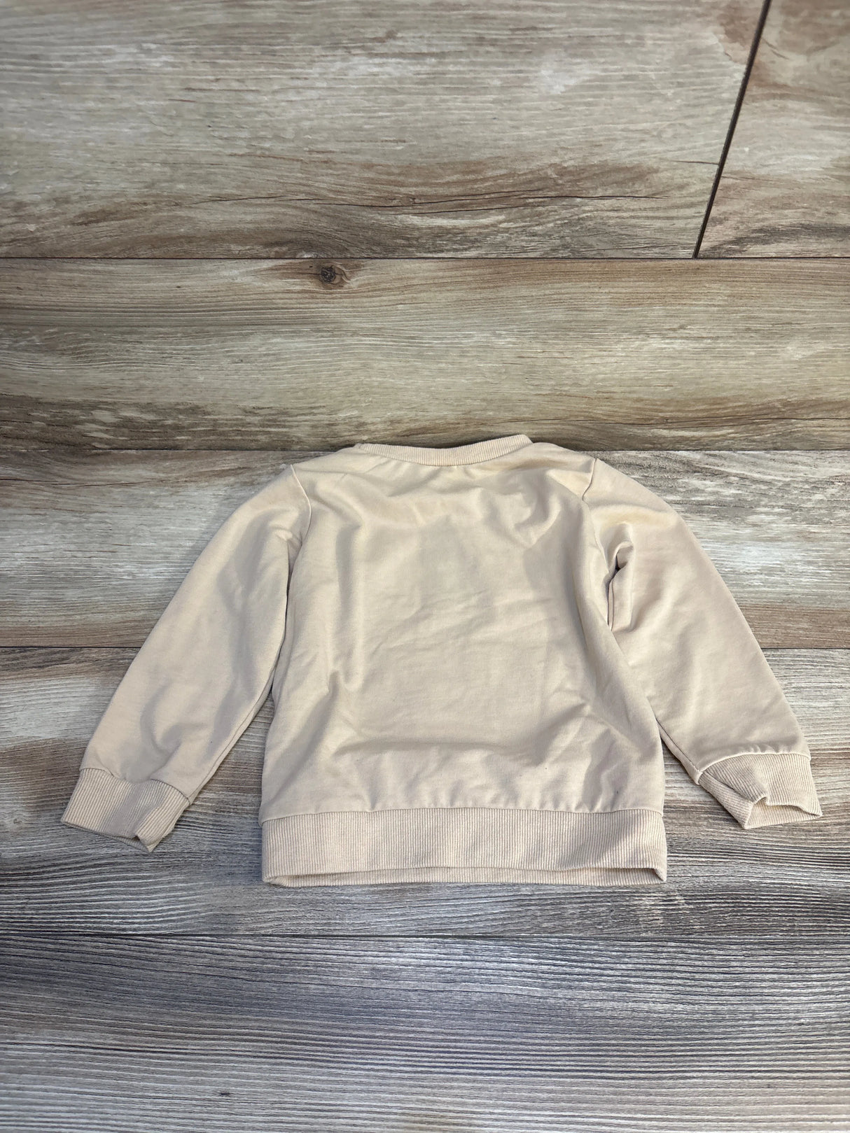 Beige long sleeve kids sweatshirt laid flat on wood background, children's clothing resale