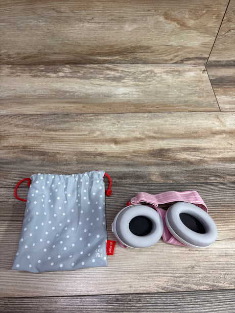 Top view of Alpine Muffy Baby noise cancelling ear muffs in white and pink beside a gray polka dot pouch on wood