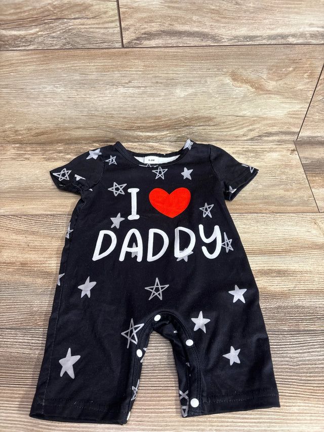 Flat lay of black shortie baby romper (6–9M) with red heart and white 'I DADDY' print, gray stars and crotch snap closures on wood floor