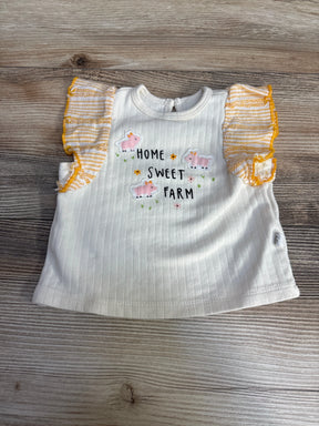Flat lay of cream infant shirt with 'Home Sweet Farm' embroidery, pink sheep and yellow ruffle sleeves on wood background