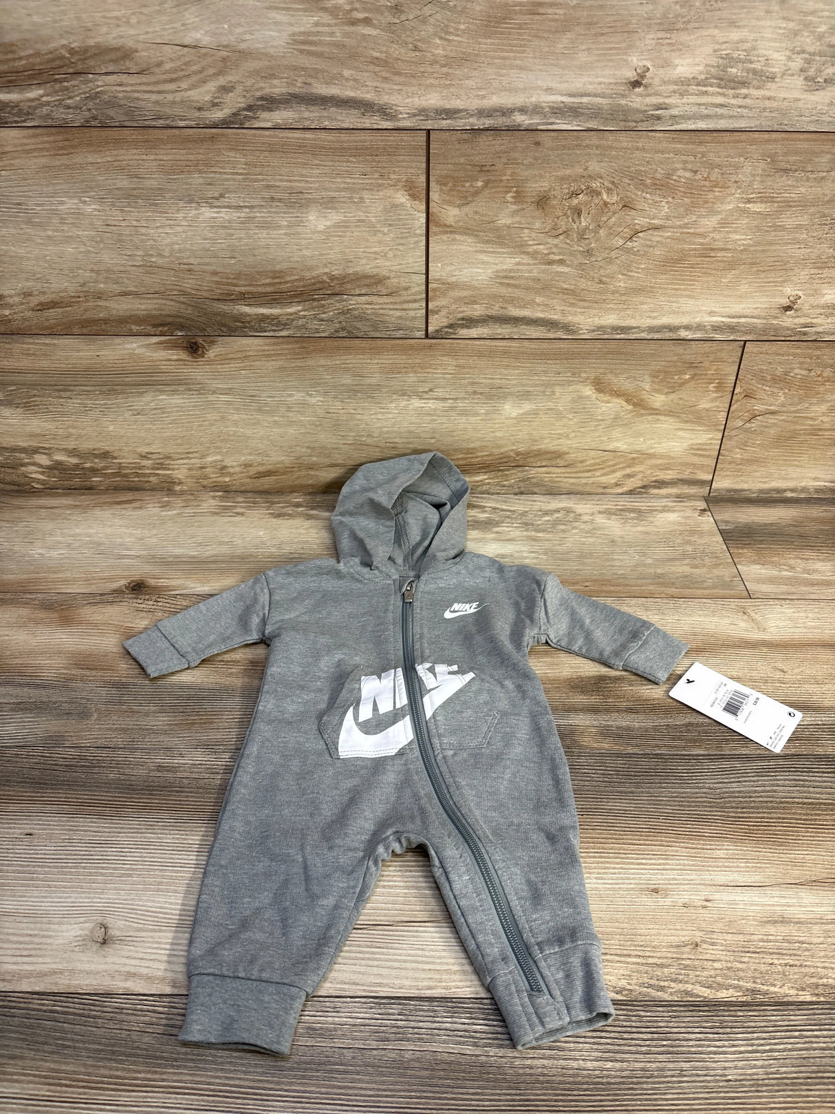 Top-down view of grey Nike hooded baby coverall (3M) showcasing front zipper and white Nike logo on wood floor background
