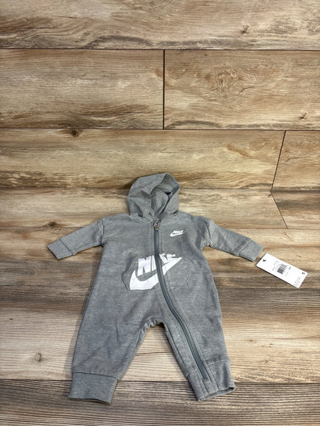 Top-down view of grey Nike hooded baby coverall (3M) showcasing front zipper and white Nike logo on wood floor background