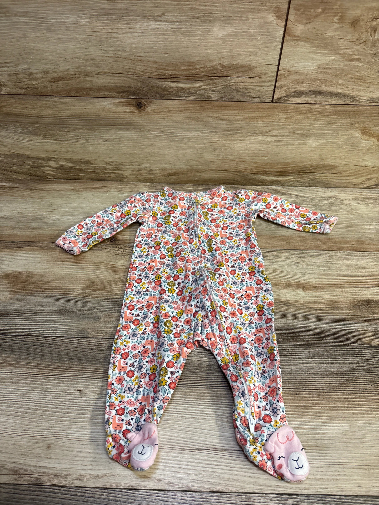 Front view of a Simple Joys sleeper showcasing floral print, long sleeves, and footed legs on a wood floor