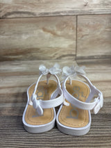Front view of white Bebe toddler chiffon flower sandals showing flower accents and buckled ankle straps on wood background