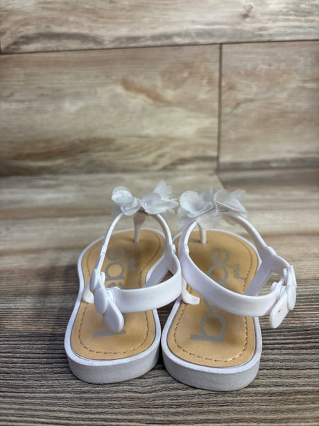 Front view of white Bebe toddler chiffon flower sandals showing flower accents and buckled ankle straps on wood background