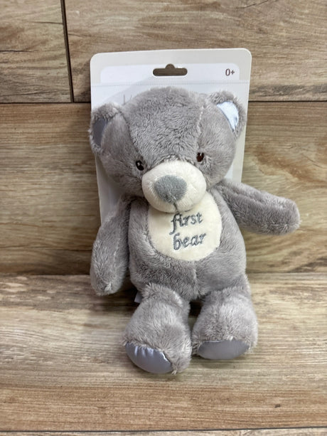 Front view of 10 inch gray KellyBaby My First Bear plush toy with First bear text on belly, packaged on a wood background