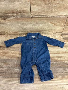 Blue denim long-sleeve baby romper laid flat on wooden floor, with button front and chest pockets