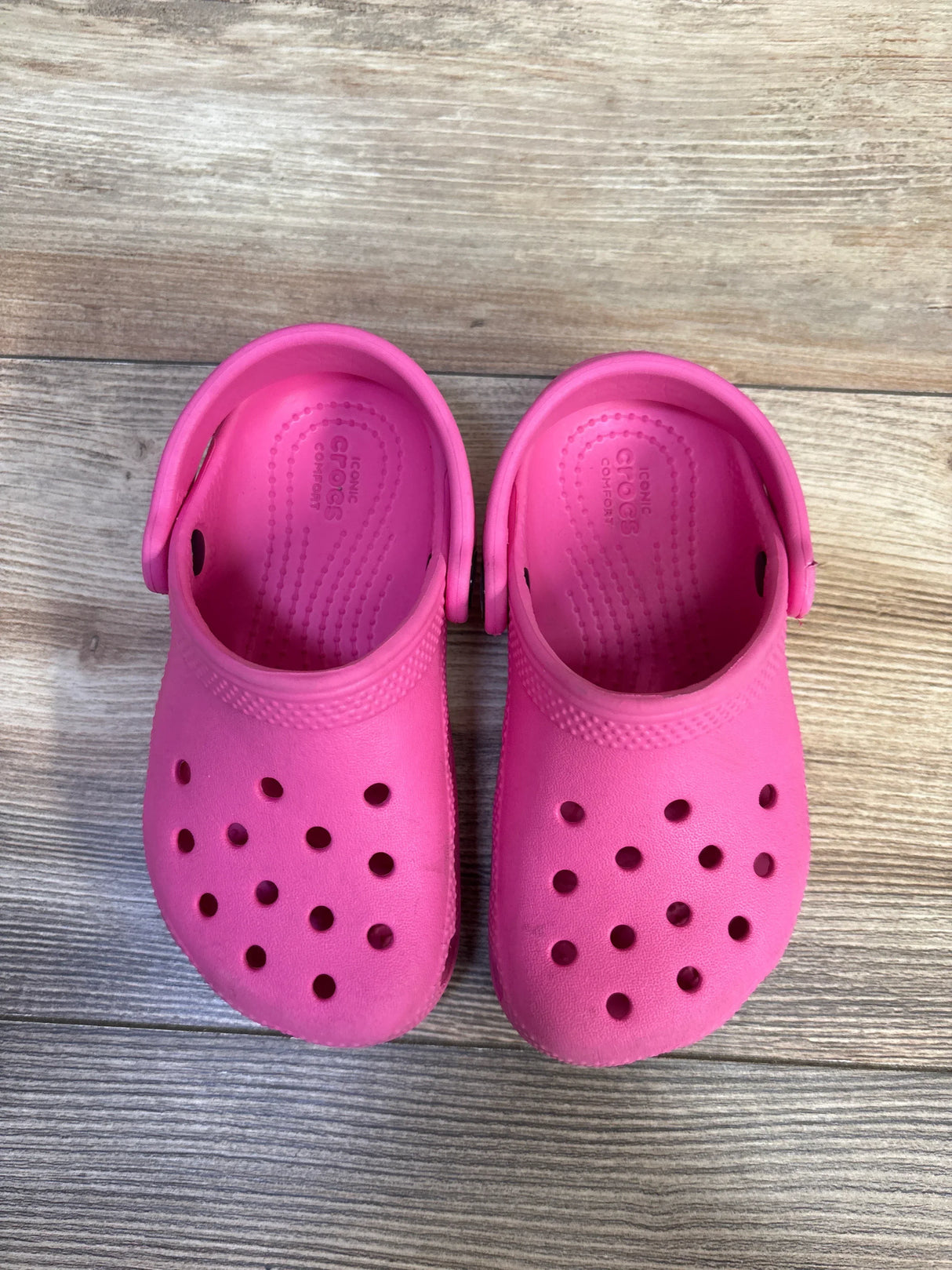 Top-down view of pink Crocs Classic clogs size 9C showing ventilation holes, heel straps, and textured footbeds on a wood floor