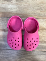 Top-down view of pink Crocs Classic clogs size 9C showing ventilation holes, heel straps, and textured footbeds on a wood floor
