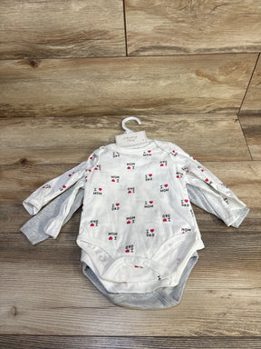 Flat lay of 3-pack long-sleeve baby bodysuits: white bodysuit printed I heart Mom and I heart Dad, with gray and white basics on wood