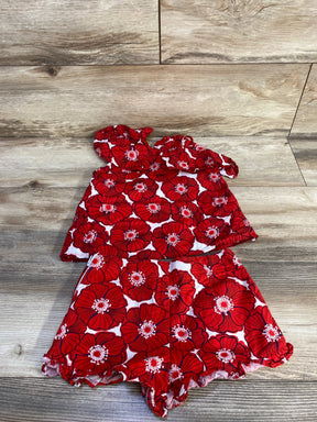 Flat lay of toddler two-piece red poppy-print sun top and ruffle-hem shorts showing floral pattern and ruffle hems on light wood background