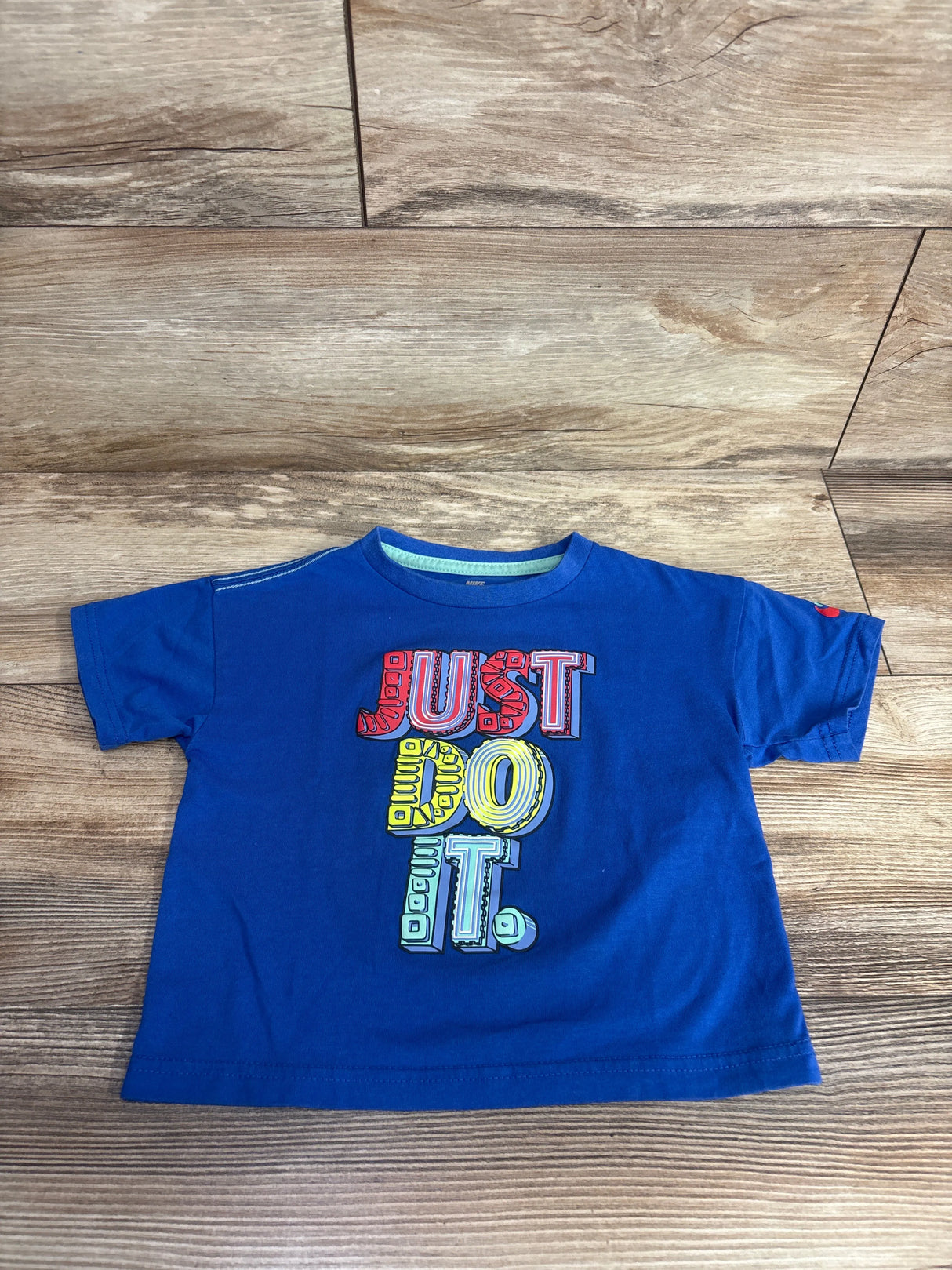 Blue toddler t-shirt with colorful textured letters spelling Just Do It on wooden floor
