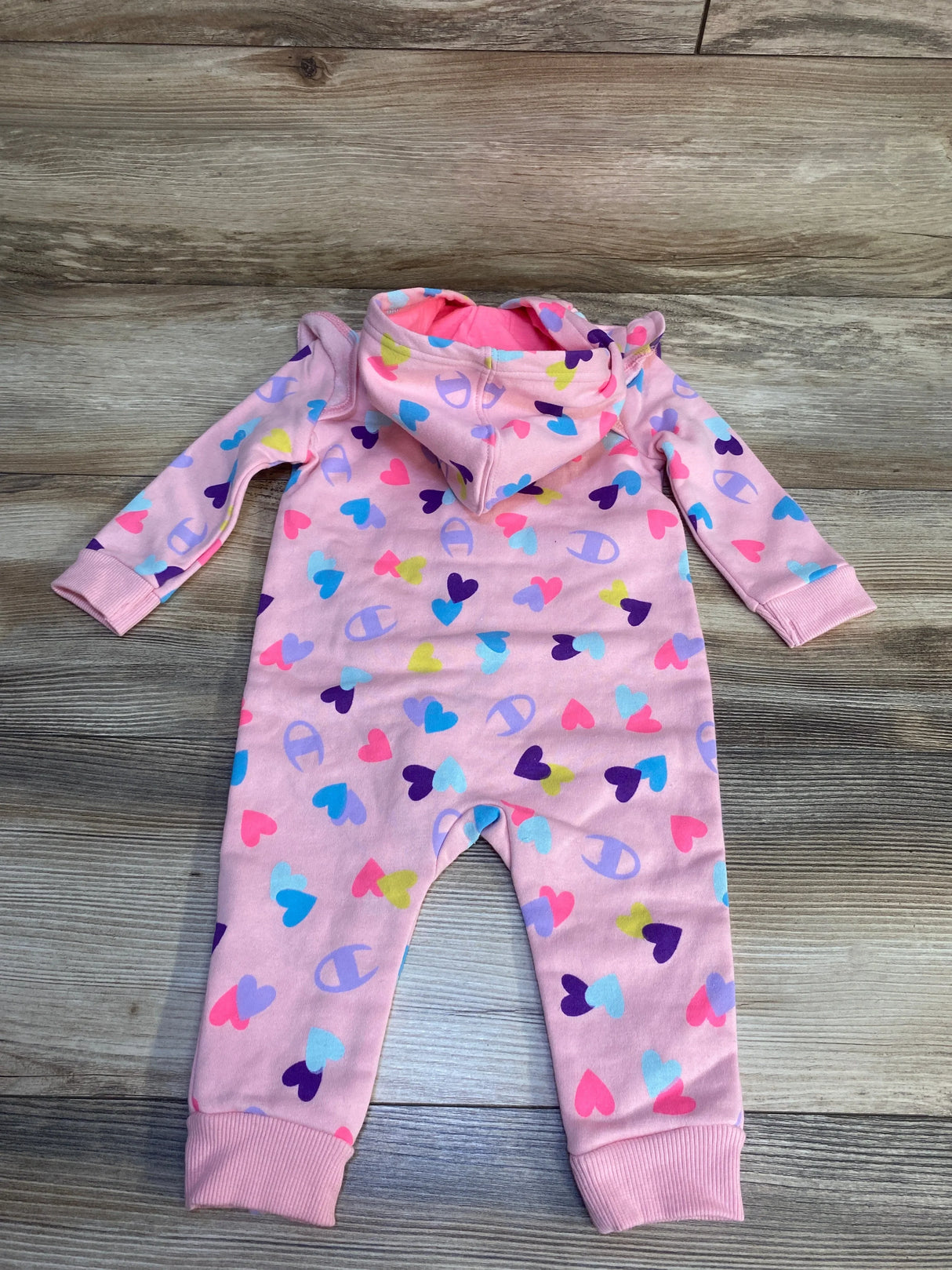 Pink baby hooded romper with colorful heart pattern on wood floor