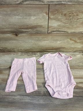 Overhead view of a pink ribbed bodysuit and pants set showcasing short sleeves and snap closures on a wood-look background