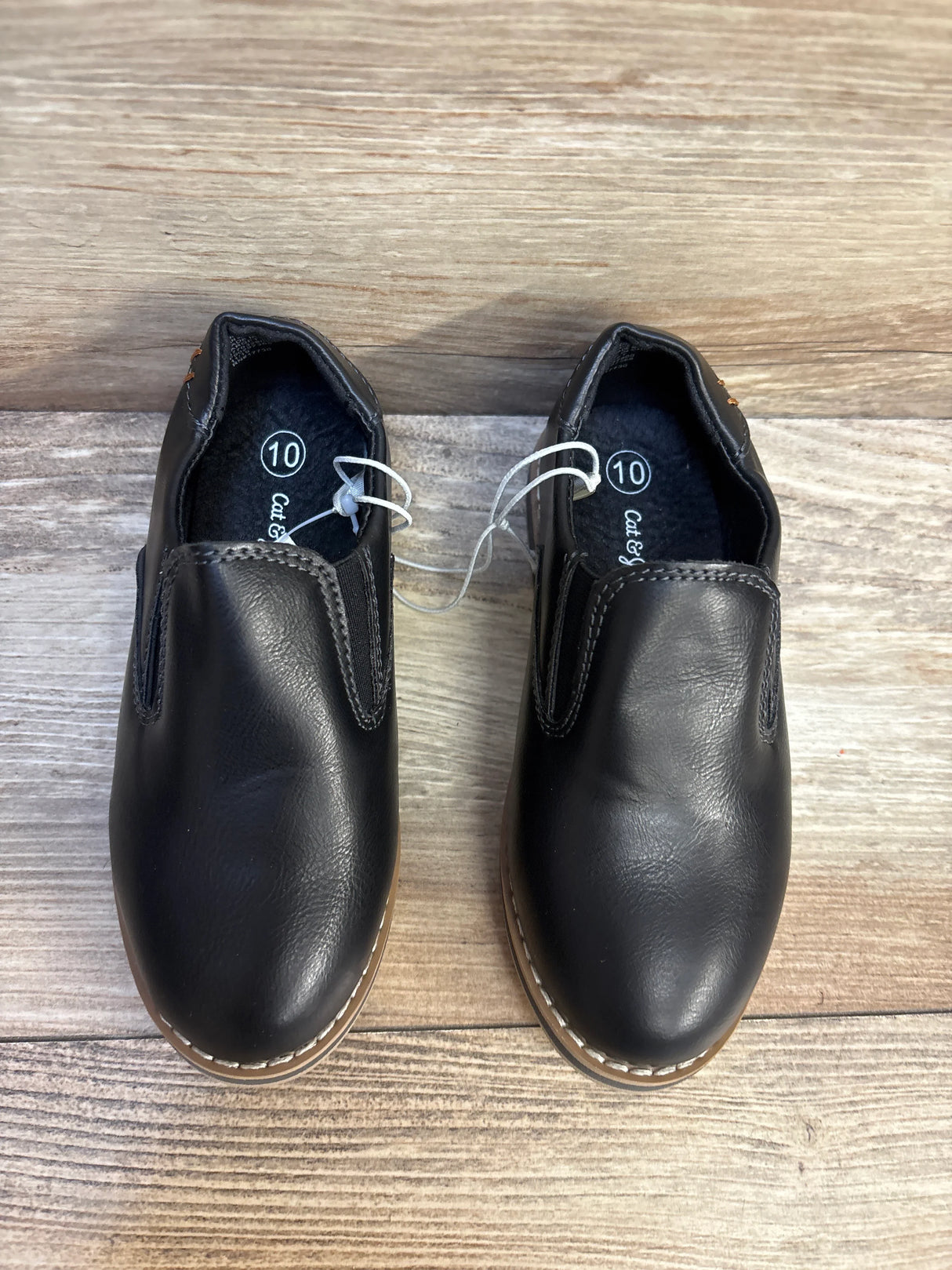 Black slip-on boys shoes size 10 with tan soles on wood background