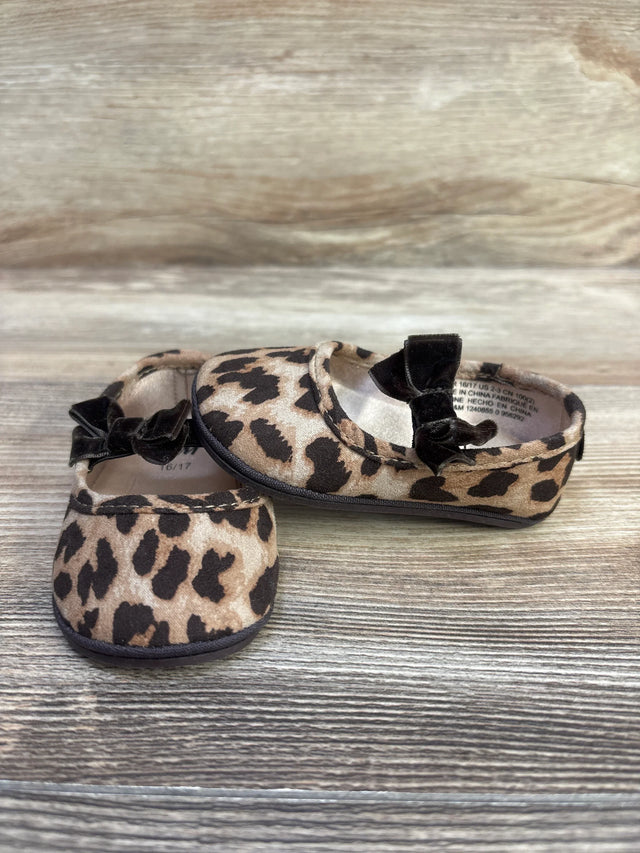 Front and side view of leopard-print baby ballet flats showcasing black velvet bows and rounded toes on a light wood surface