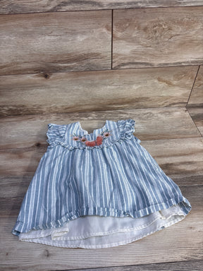 Flat lay of blue and white striped toddler top showcasing embroidered floral yoke, ruffled cap sleeves, and layered white lining on wood floor background