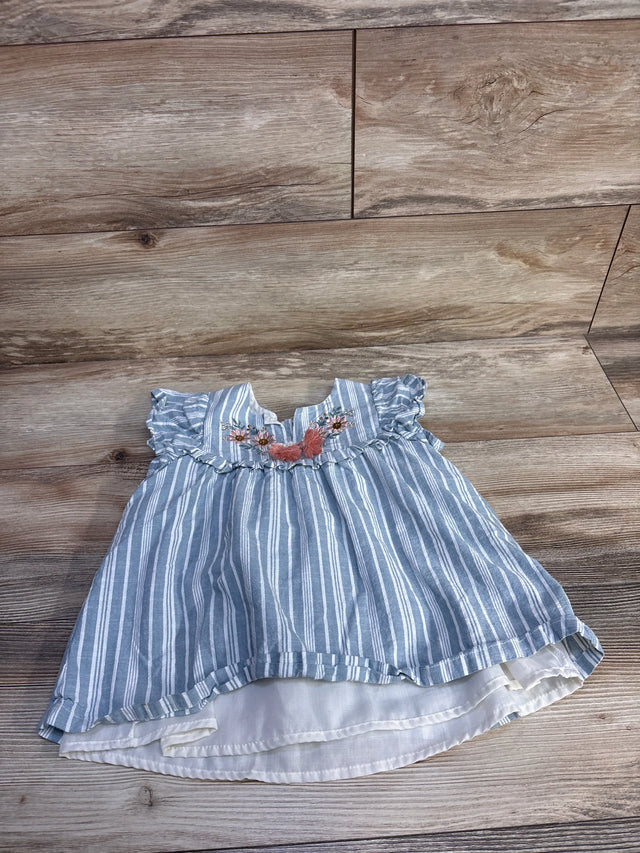 Flat lay of blue and white striped toddler top showcasing embroidered floral yoke, ruffled cap sleeves, and layered white lining on wood floor background