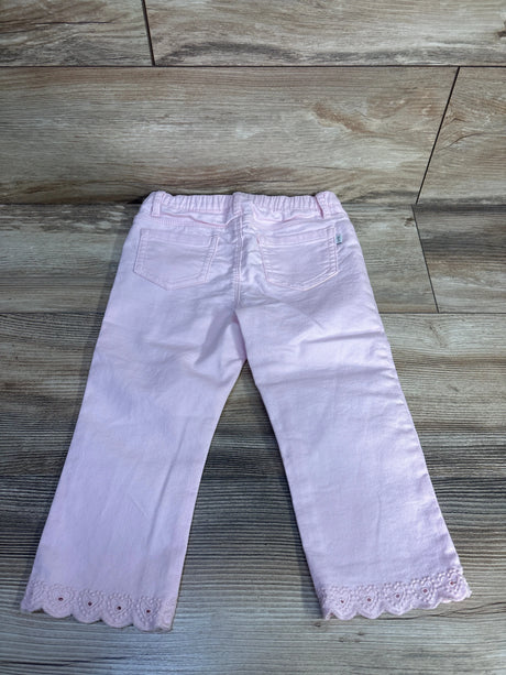 Back view of Oshkosh jeans showcasing light pink denim with eyelet embroidered hem trim and back pockets on wood plank floor