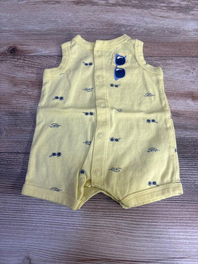 Top-down view of yellow newborn shortie romper with navy sunglass prints, front snap closure, sunglass patch on wood surface