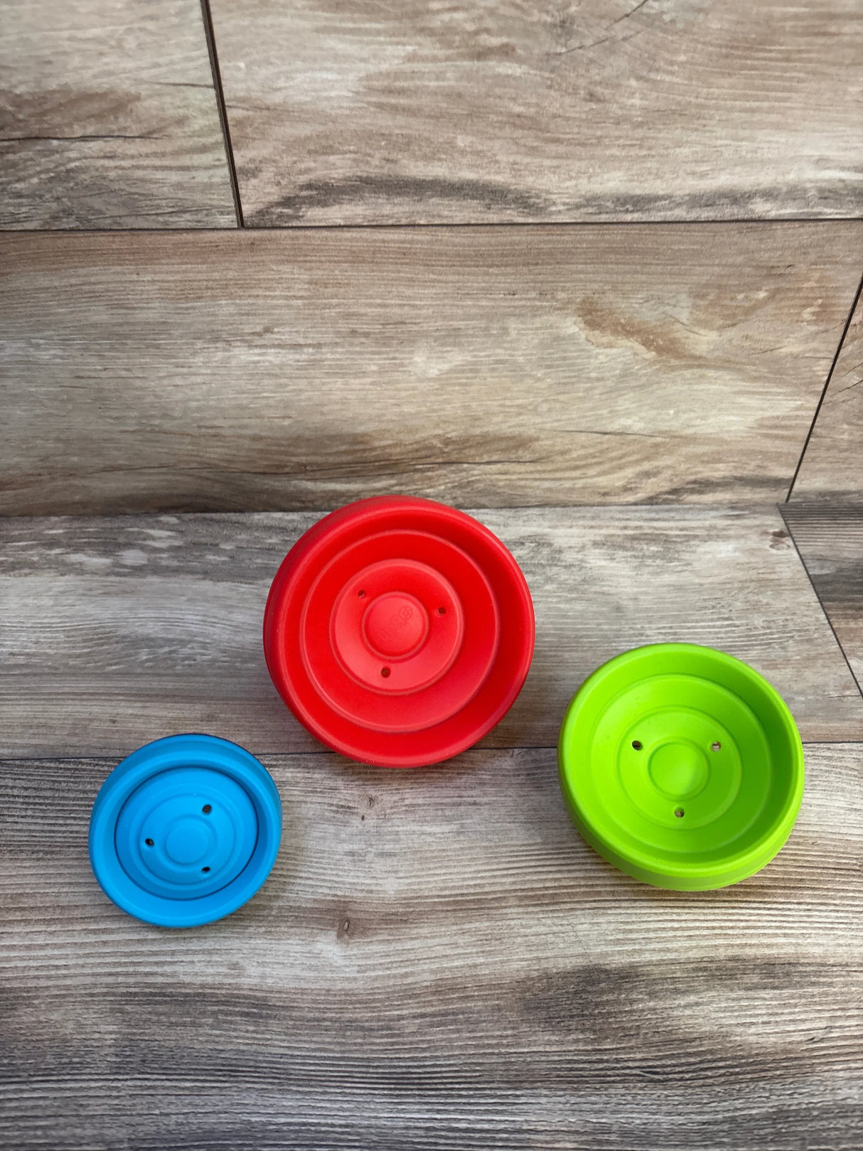 Top-down view of Bright Starts Oball Flex & Stack Balls three pack showcasing three flexible nesting discs in red, green, and blue on a wood plank background