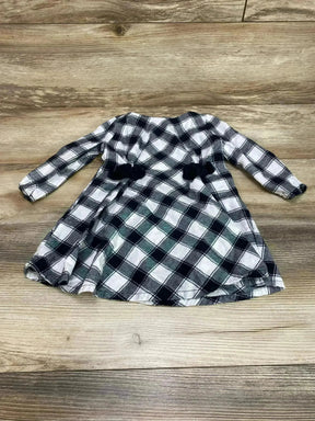 Flat lay of white and black buffalo check baby dress showcasing long sleeves and two black waist bows on a wood background
