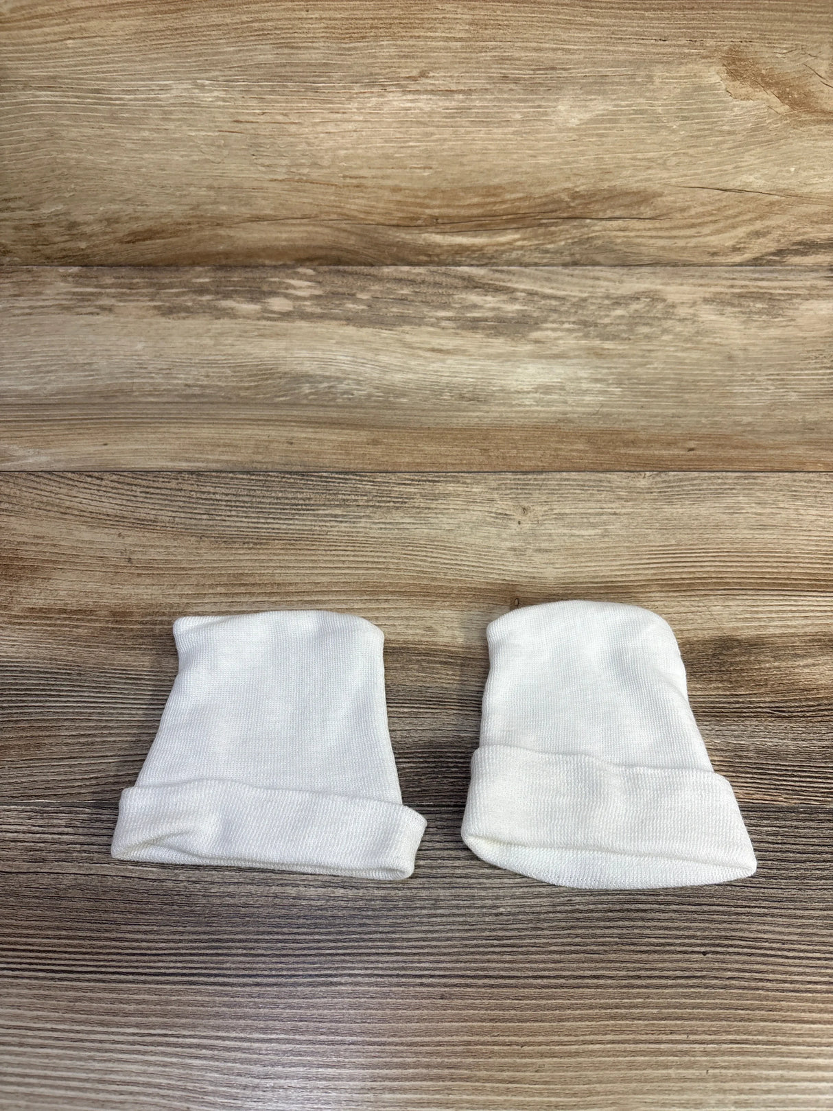 Top-down view of two white preemie fold-over baby hats showcasing rolled cuffs on wood background